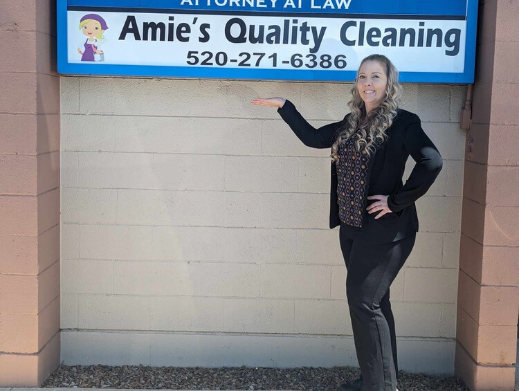 Amie the owner, standing by the Amie's Quality Cleaning sign with her hand up.